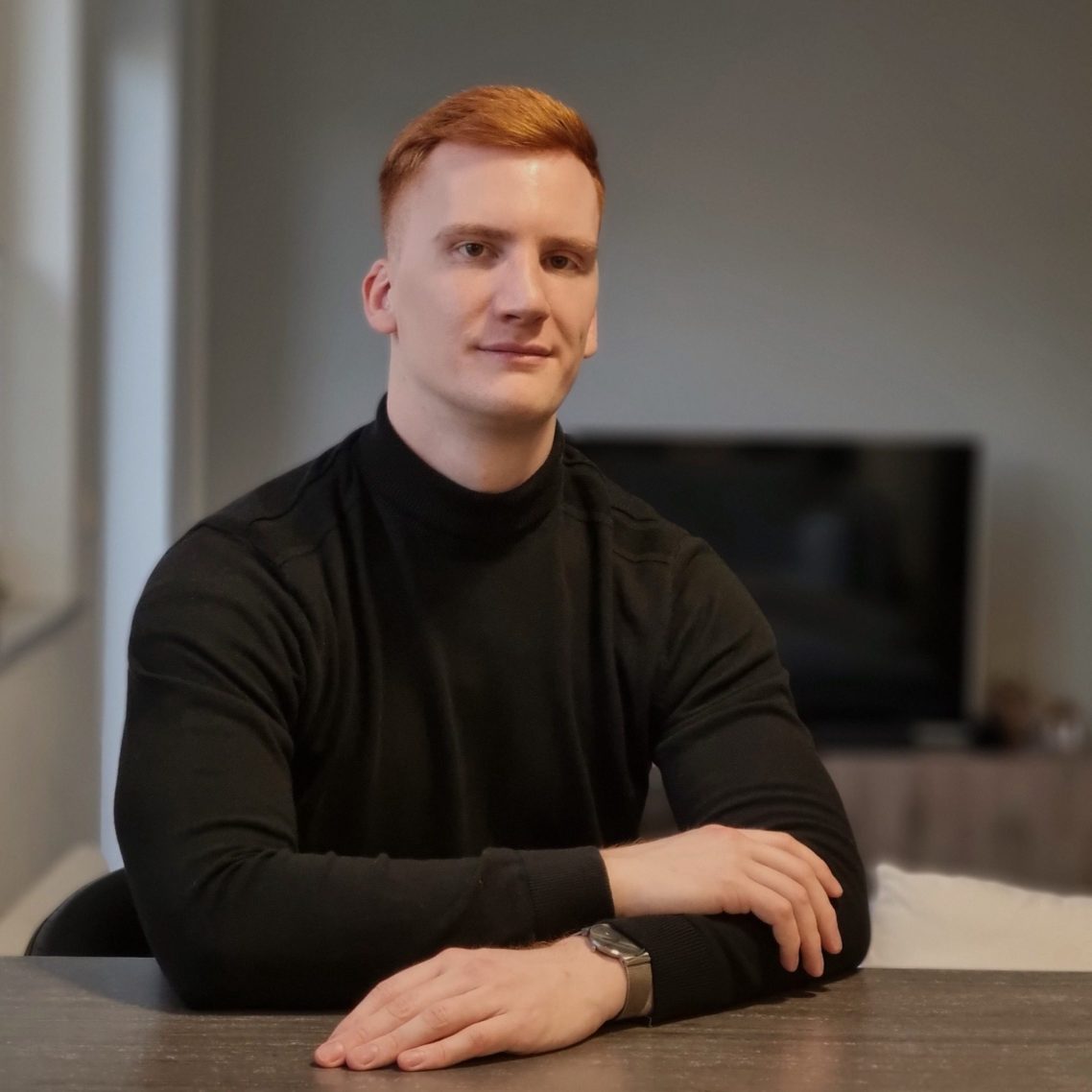 Jonas Klar – Portraitfoto; sitzend im schwarzen Rollkragenpullover