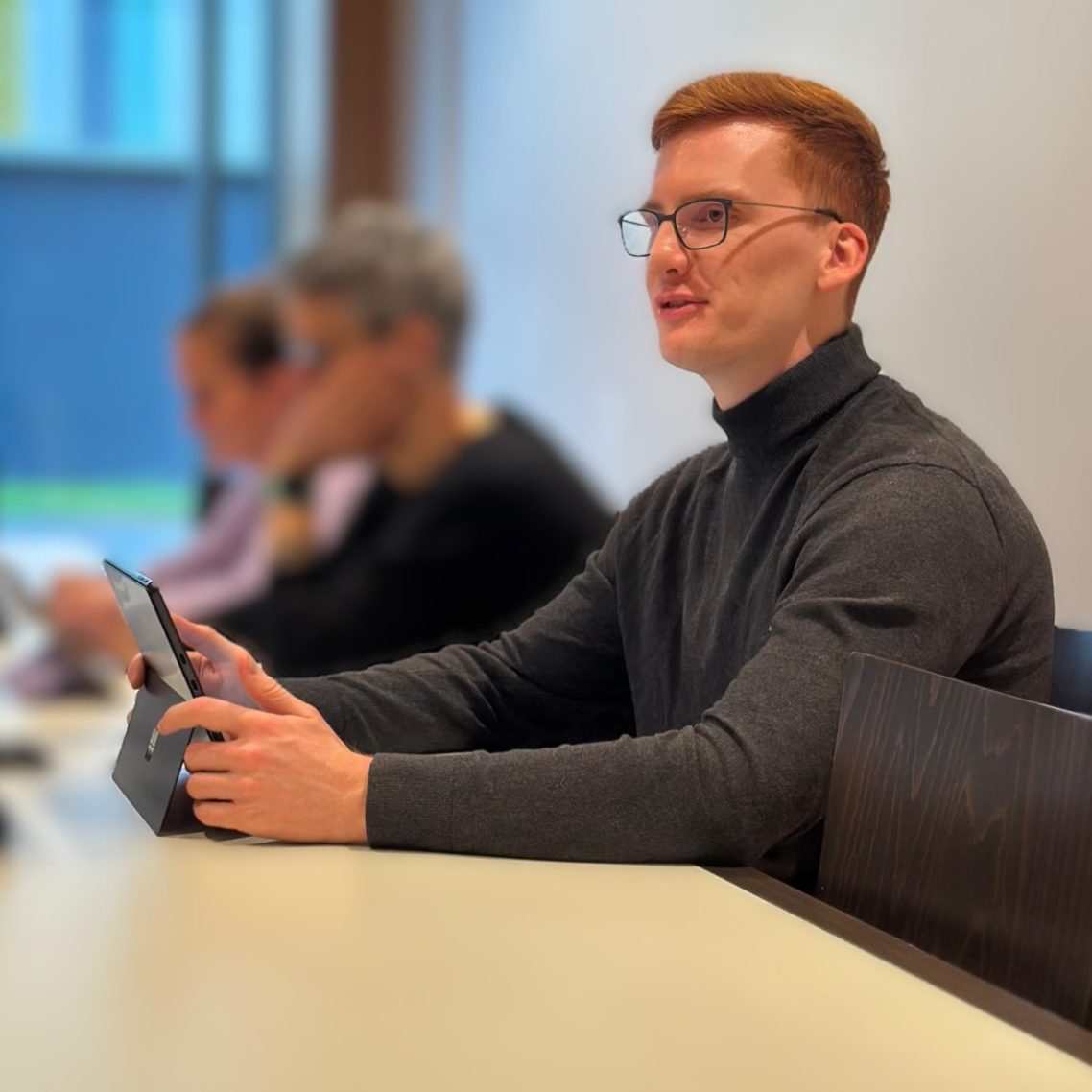 Jonas Klar als engagierter Kommunalpolitiker – im Gespräch mit Kollegen am Sitzungstisch, Laptop vor sich, konstruktiver Austausch